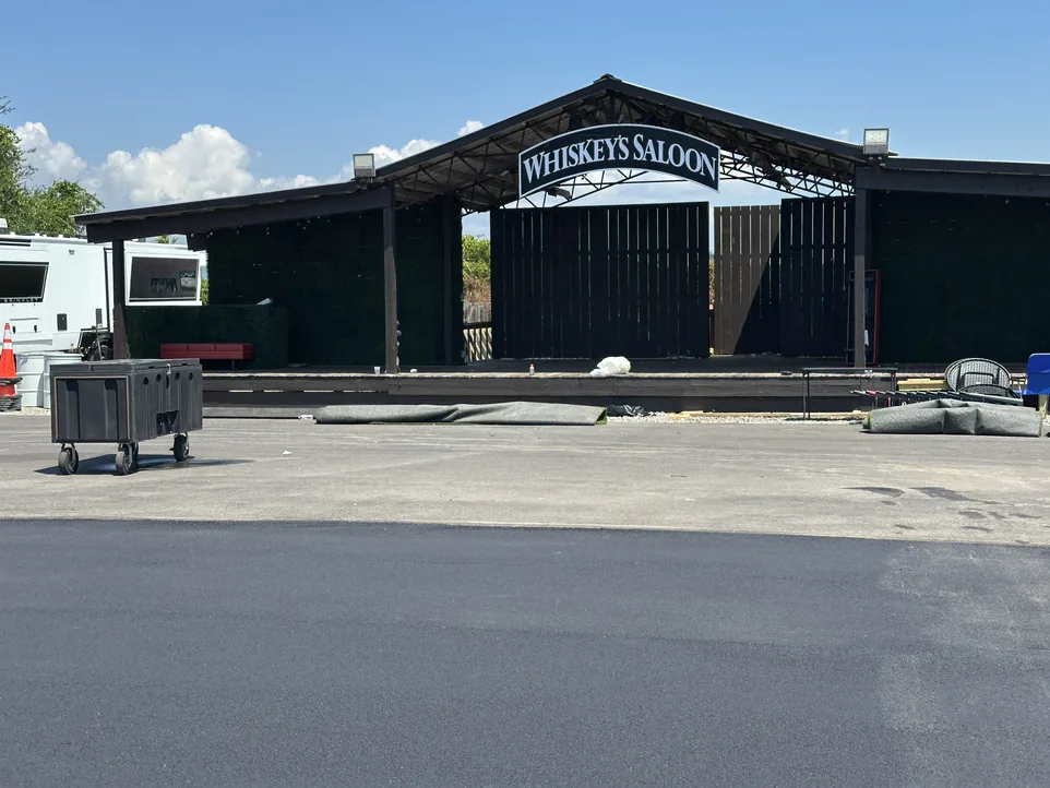 A large patch repair in the center of an asphalt lot in front of a stage